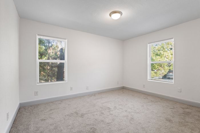 Bright and airy bedroom with large windows overlooking greenery, featuring soft carpet flooring and modern lighting.
