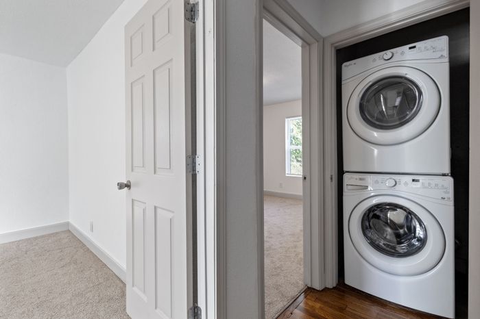 Bright hallway featuring a stacked washer and dryer, leading to a cozy carpeted room with ample natural light.