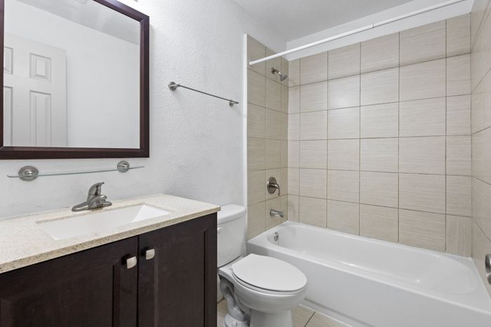 Modern bathroom featuring sleek dark wood vanity, spacious mirror, and elegant tiled bathtub area.