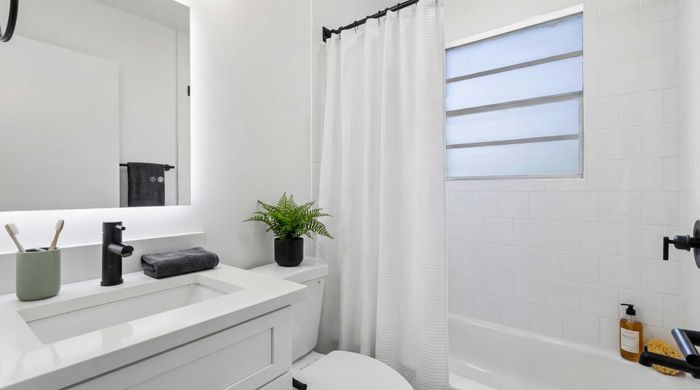 Elegant bathroom with a modern white vanity, black faucet, and a soft lighting mirror; features a lush green plant and cozy decor in a stylish space.