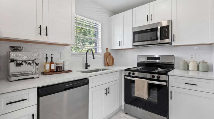 Chic modern kitchen featuring sleek white cabinetry, high-end stainless steel appliances, and an elegant coffee station.