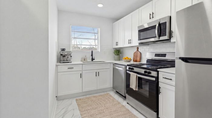 Modern kitchen with sleek white cabinetry, stainless steel appliances, and a chic espresso machine under bright, natural light.