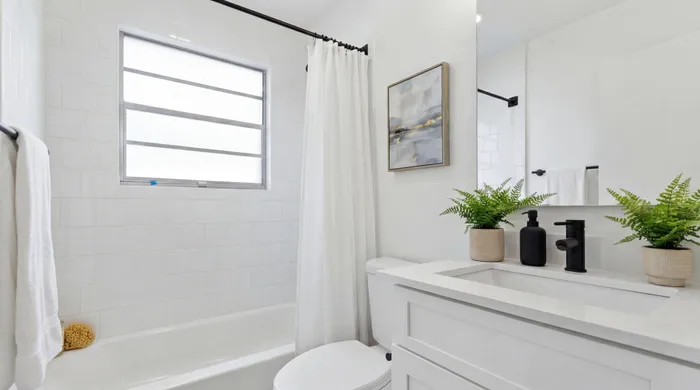 Bright, modern bathroom with elegant white tiles, contemporary artwork, and lush green plants.