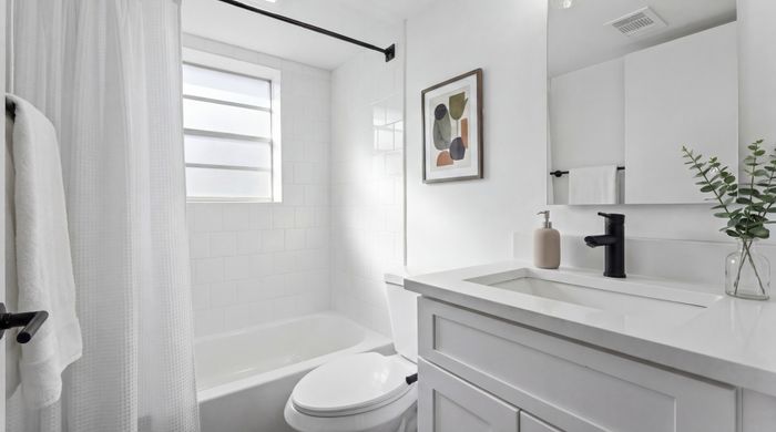 Bright and modern bathroom featuring elegant white tiles, a sleek vanity with black fixtures, and a stylish abstract painting.