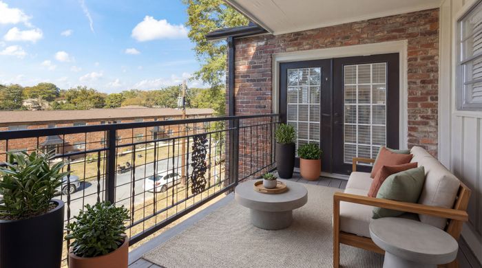 Charming balcony with rustic brick walls, cozy seating, and lush greenery offering a serene outdoor retreat.