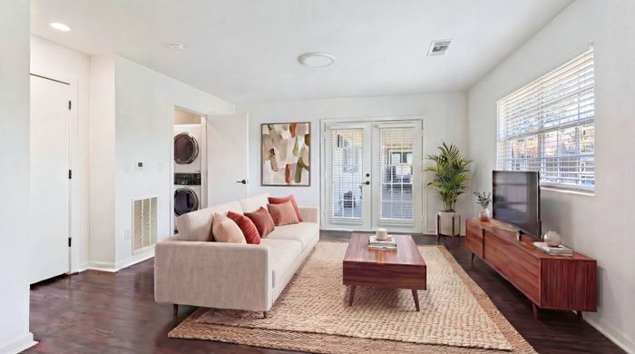 Bright and modern living room featuring elegant furnishings, a stylish sofa with warm throw pillows, and chic decor, complemented by natural light from large windows and French doors.