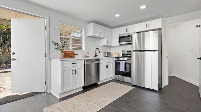 Modern kitchen with sleek white cabinetry, stainless steel appliances, and a bright open doorway leading outdoors.