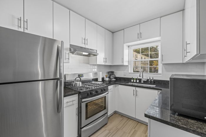 Sleek modern kitchen with stainless steel appliances, bright white cabinetry, and elegant black countertops.