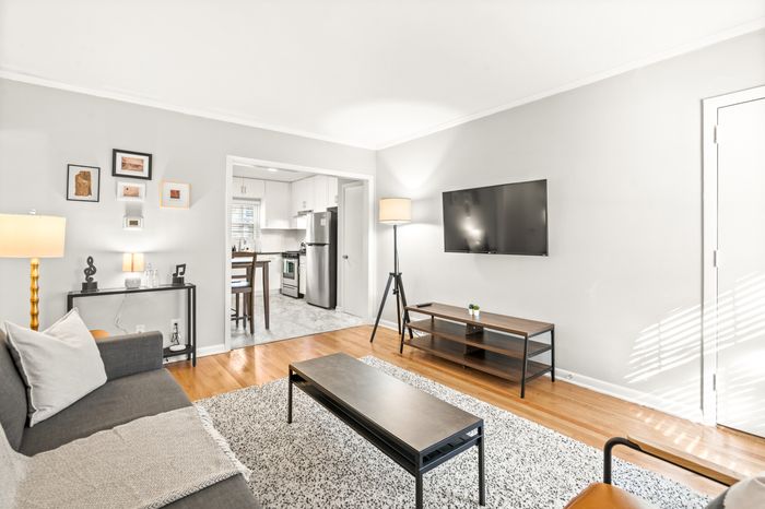 Bright and stylish living room with cozy sofa, wall-mounted TV, and a peek into a modern kitchen. Inviting and well-lit space with contemporary decor.