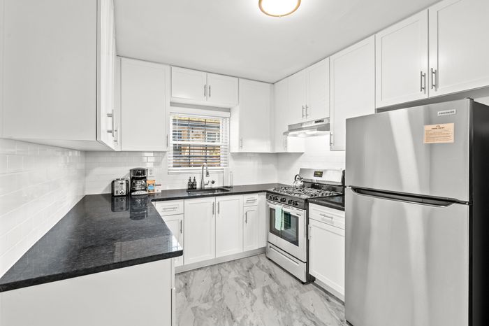 Bright modern kitchen with stainless steel appliances, sleek black countertops, and white cabinetry.