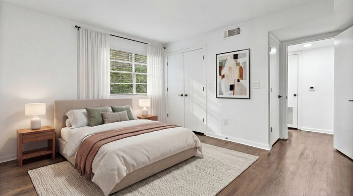 Bright and spacious bedroom with elegant decor, featuring large windows, modern art, and hardwood floors.
