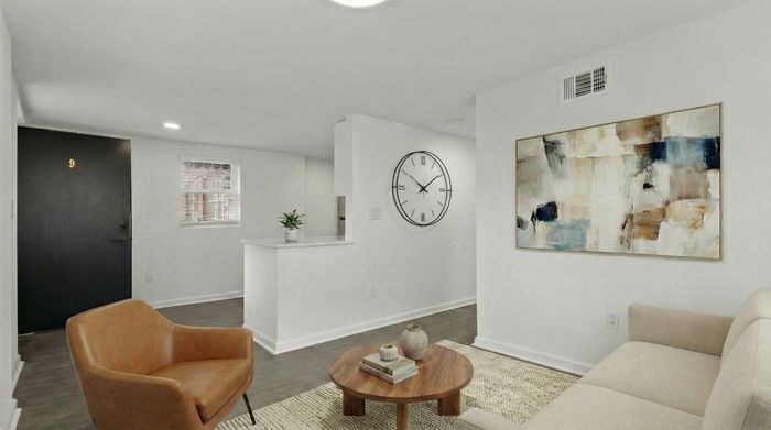 Elegant living area featuring modern decor with a large abstract painting and stylish clock on white walls, comfy seating, and a chic wooden coffee table.