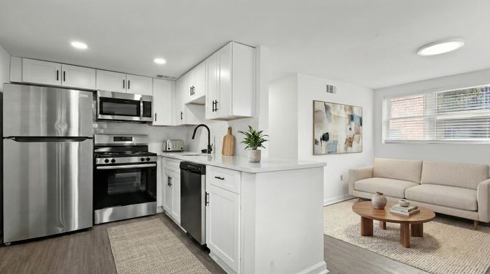 Chic open-plan kitchen and living area featuring modern stainless steel appliances, elegant white cabinetry, and cozy seating with natural light.