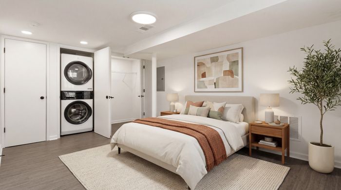 Elegant bedroom featuring a cozy bed with warm-toned bedding, stylish nightstand, and in-room laundry with a washer and dryer set.