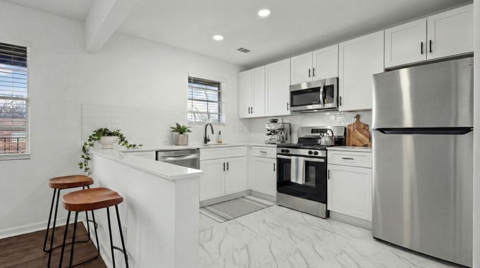 Bright, modern kitchen with sleek white cabinets, stainless steel appliances, and cozy breakfast bar seating.