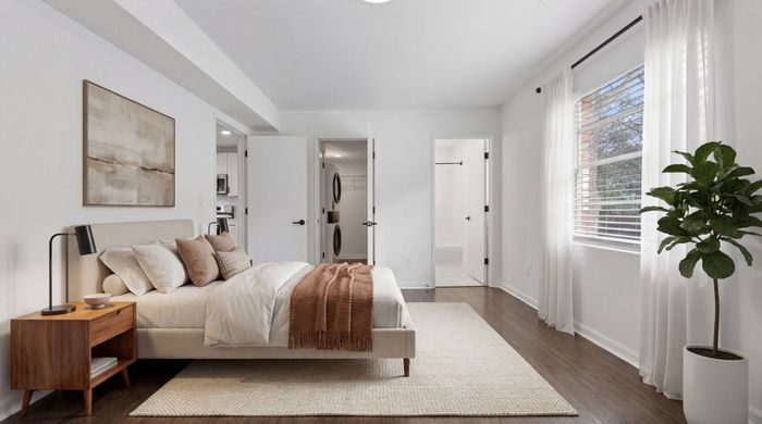 Bright and airy bedroom with elegant decor, featuring a cozy bed, wooden nightstand, stylish artwork, and abundant natural light through large windows.