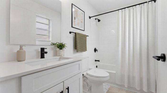 Elegant bathroom with modern fixtures, featuring a sleek white vanity, chic black accents, and a cozy bathtub with a stylish shower curtain.