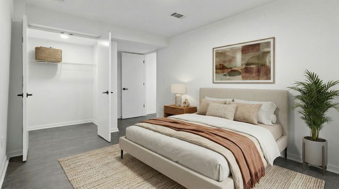 Elegant bedroom featuring a cozy bed, stylish artwork, and ample closet space, complemented by a warm bedside lamp and a touch of greenery.