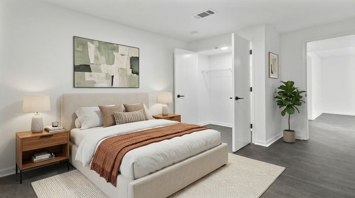 Elegant bedroom featuring a cozy bed with textured pillows and a warm throw, flanked by stylish bedside tables and ambient lighting, adjacent to a spacious walk-in closet and a lush indoor plant.