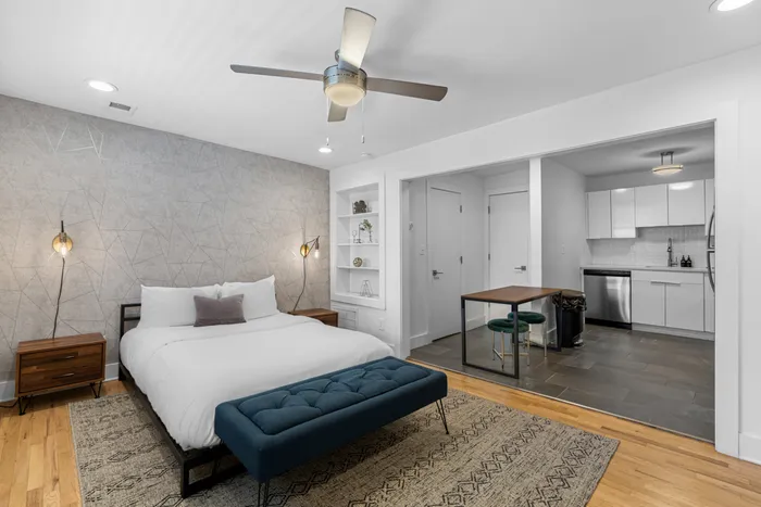 Modern studio apartment featuring a cozy bedroom area, contemporary kitchen, and stylish built-in shelves, illuminated by chic lighting and a ceiling fan.