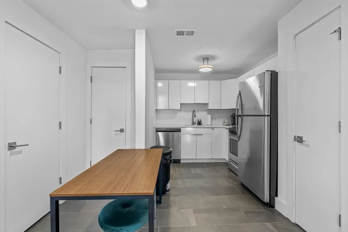Modern kitchen with sleek white cabinetry, stainless steel appliances, and a cozy dining area with a wooden table and teal cushioned stool.