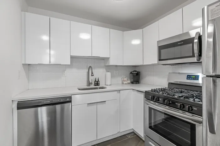 Modern kitchen with sleek white cabinetry, stainless steel appliances, and elegant countertop in a sophisticated apartment.
