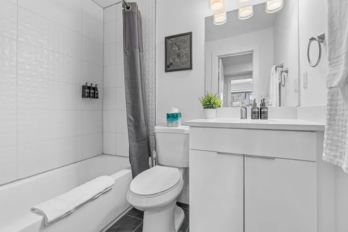 Elegant modern bathroom with sleek white fixtures, chic vanity, and stylish wall tiles, complemented by soft lighting and thoughtful décor accents.