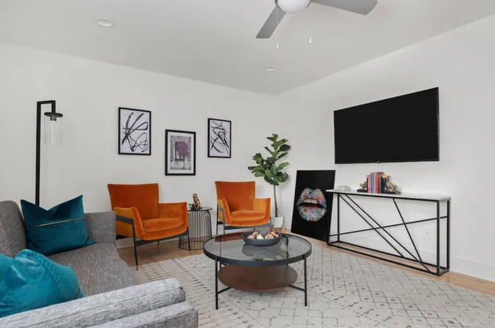 Bright and modern living room featuring sleek furniture, vibrant orange chairs, stylish decor, and a large wall-mounted TV.