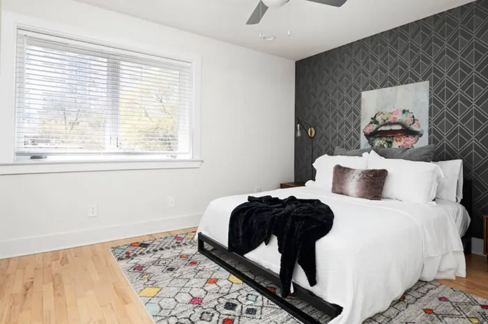 Chic, modern bedroom with a stylish dark accent wall, cozy bed, and large window providing natural light.