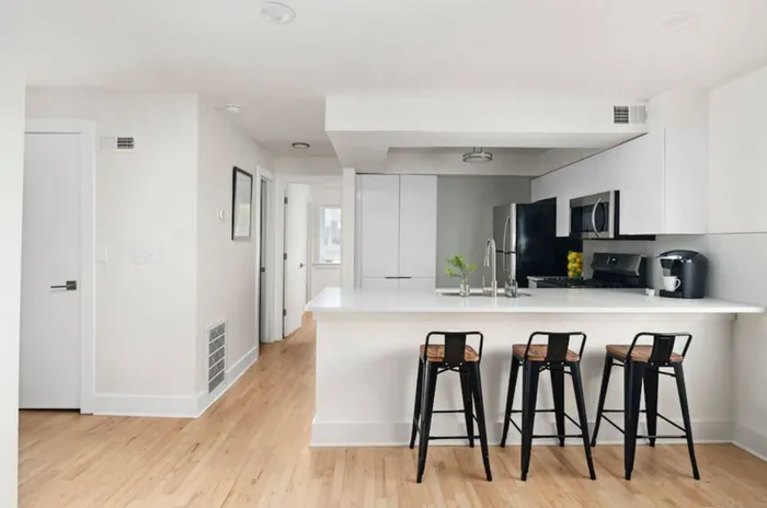 Modern kitchen area with sleek white cabinets, stainless steel appliances, and a stylish breakfast bar featuring three chic barstools.