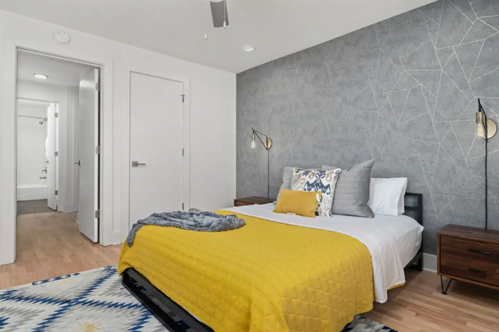 Modern bedroom featuring a stylish gray accent wall, cozy bed with yellow bedding, and elegant lighting.