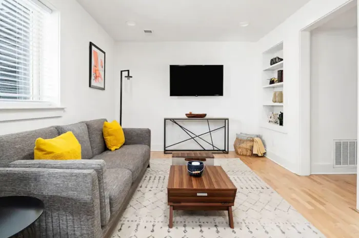 Cozy living room featuring a stylish gray sofa with vibrant yellow cushions, sleek wooden coffee table, and wall-mounted TV, perfect for relaxation and entertainment.