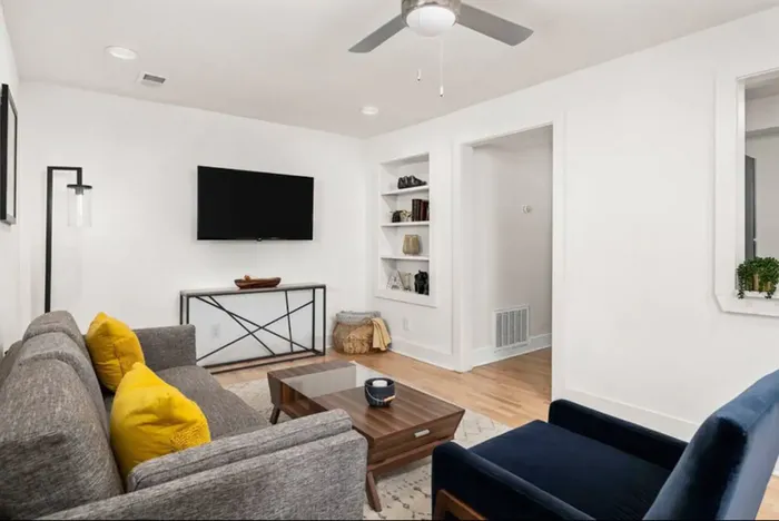 Contemporary living room with stylish gray sofa, vibrant yellow cushions, and sleek decor. Features a wall-mounted TV, coffee table, and accent chair, creating a cozy and inviting atmosphere.