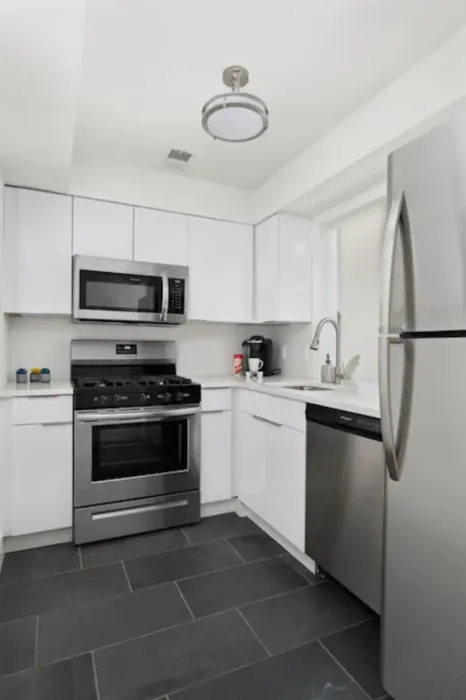 Modern kitchen with sleek white cabinetry, stainless steel appliances, and dark tile flooring.