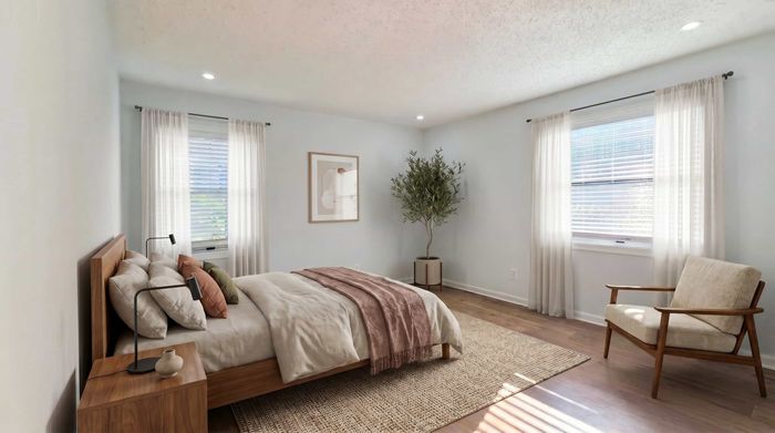 Cozy bedroom with soft lighting, featuring a plush bed, stylish wooden nightstand, and a comfortable armchair, accented by greenery and art on the wall.