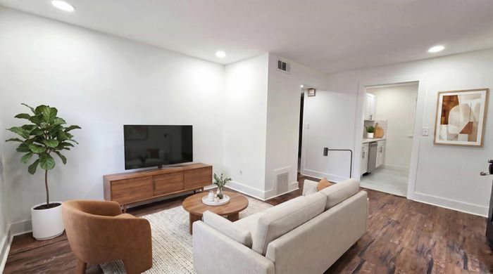 Bright and modern living room with sleek wooden floors, stylish furniture, and a minimalist kitchen view.