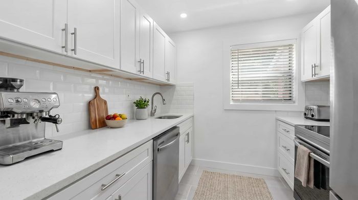 Modern kitchen with sleek white cabinetry, stainless steel appliances, and a polished countertop, featuring a coffee machine and fresh fruit for a welcoming touch.
