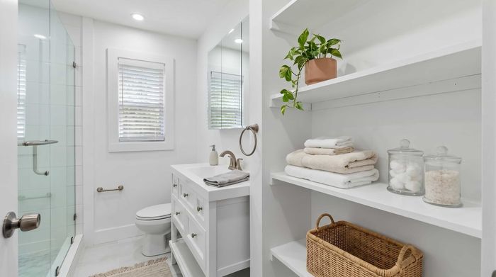 Bright and modern bathroom with sleek glass shower, stylish vanity, and ample shelving for storage, complemented by fresh white decor.
