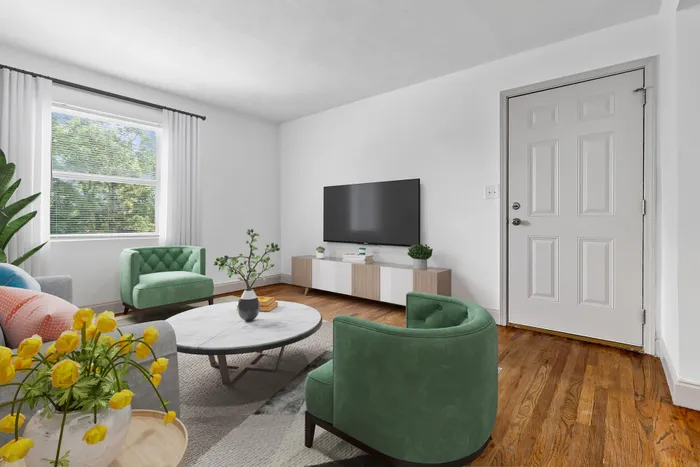 Bright living room featuring a modern design with green accent chairs, a stylish coffee table, and large TV, complemented by abundant natural light from the window.