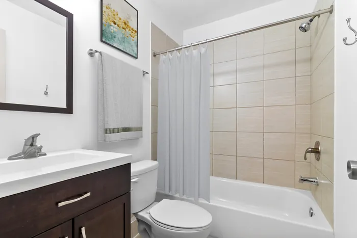 Modern bathroom featuring sleek fixtures, elegant dark wood vanity, and a clean white bathtub with stylish tile surround.