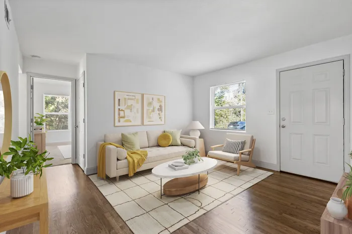 Inviting living room filled with natural light, featuring a cozy beige sofa, stylish accents, and lush greenery on hardwood floors.