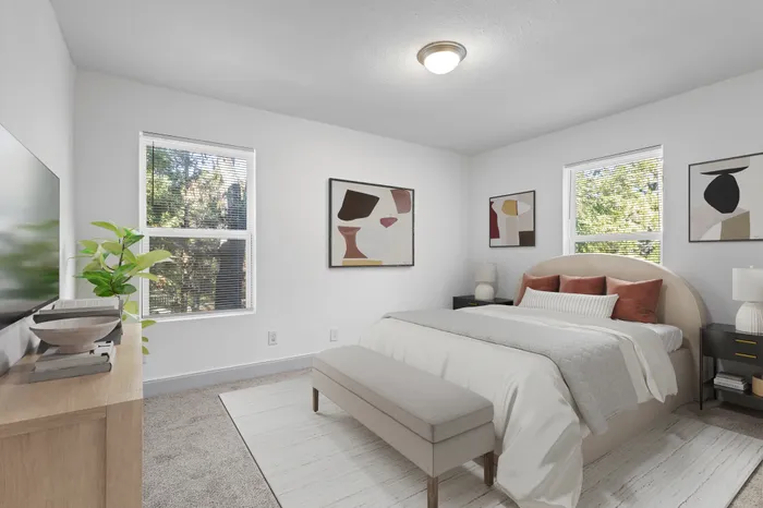 Inviting bedroom with plush bed, earthy tones, modern art, and sunlit windows overlooking greenery.