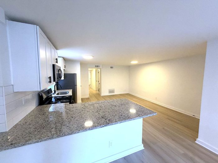 Bright and airy open-concept kitchen with elegant granite countertops, leading into a spacious and inviting living area with modern flooring.