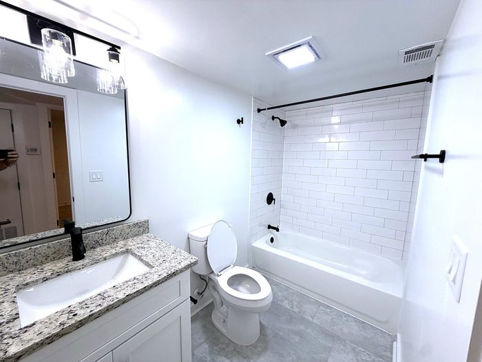 Modern bathroom with sleek granite countertop, elegant black fixtures, a stylish mirror, and pristine white subway tiles.
