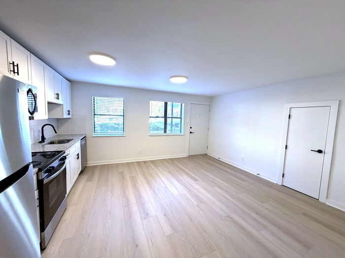 Bright and modern open-concept kitchen and living area featuring sleek stainless steel appliances, stylish cabinetry, and large windows for abundant natural light.