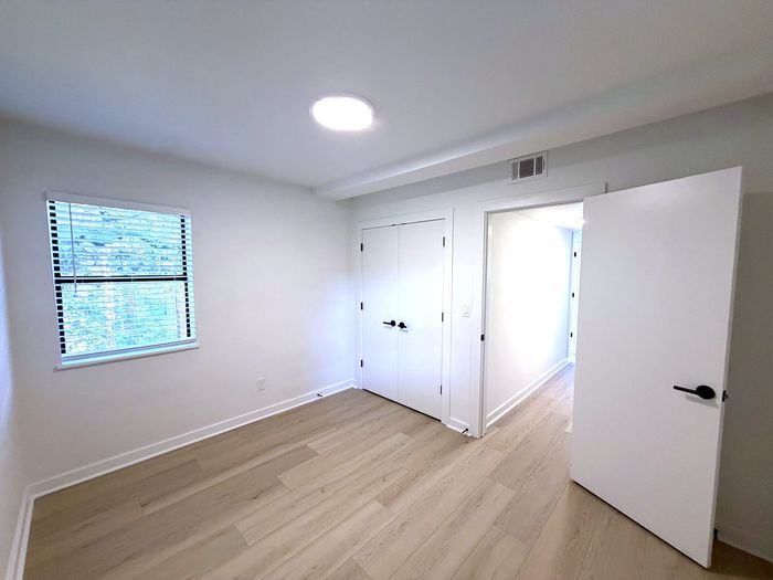 Bright and inviting, this bedroom features sleek hardwood floors, modern white doors, and a window letting in natural light.