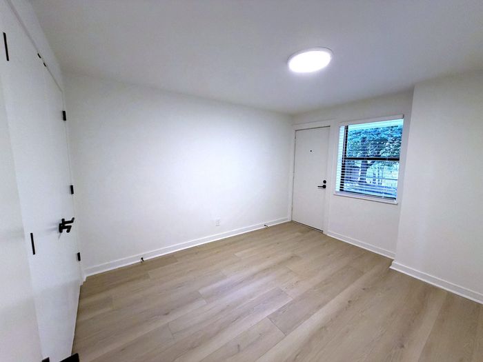 Bright, modern room with fresh, neutral walls and sleek hardwood flooring, ideal for a cozy bedroom or stylish office space with a window view.