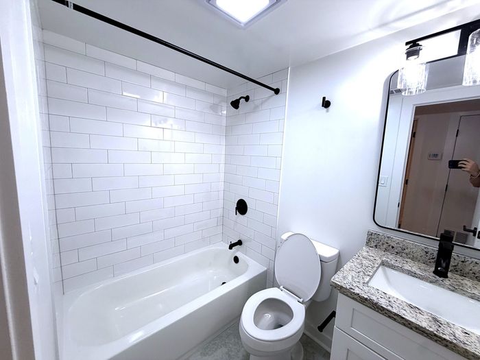 Modern bathroom featuring sleek white tiles, a luxurious bathtub, granite countertop, and elegant lighting fixtures.