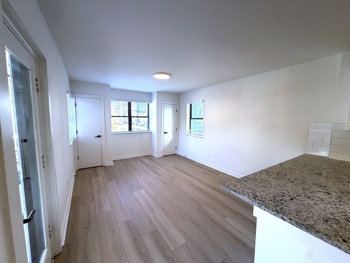 Bright and spacious living area with elegant hardwood floors and abundant natural light, featuring a sleek granite countertop in the kitchen.