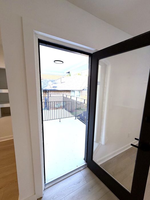 Modern apartment entrance with sleek glass door opening to a spacious balcony with a charming outdoor view.